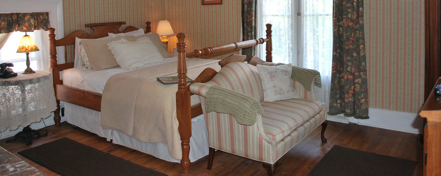 A guest room at Seven Wives Inn with a carved four-poster bed, striped settee and period wallpaper