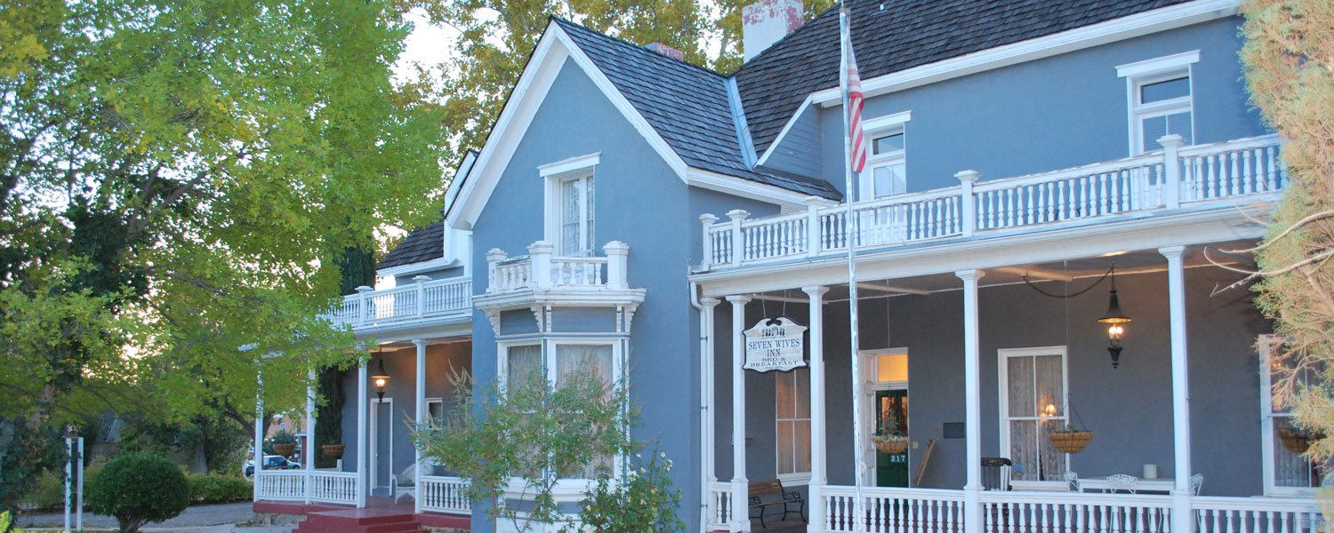 The main house at Seven Wives Inn in St. George, Utah, seen from the street, with its two-storey porch and hanging bed and breakfast sign